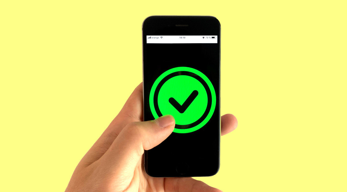 yellow background with hand holding cellphone. on phone screen is a green circle and checkmark, indicating an online poker site or poker app is good trustworthy choice where your personal info and financial data will be safe and protected.